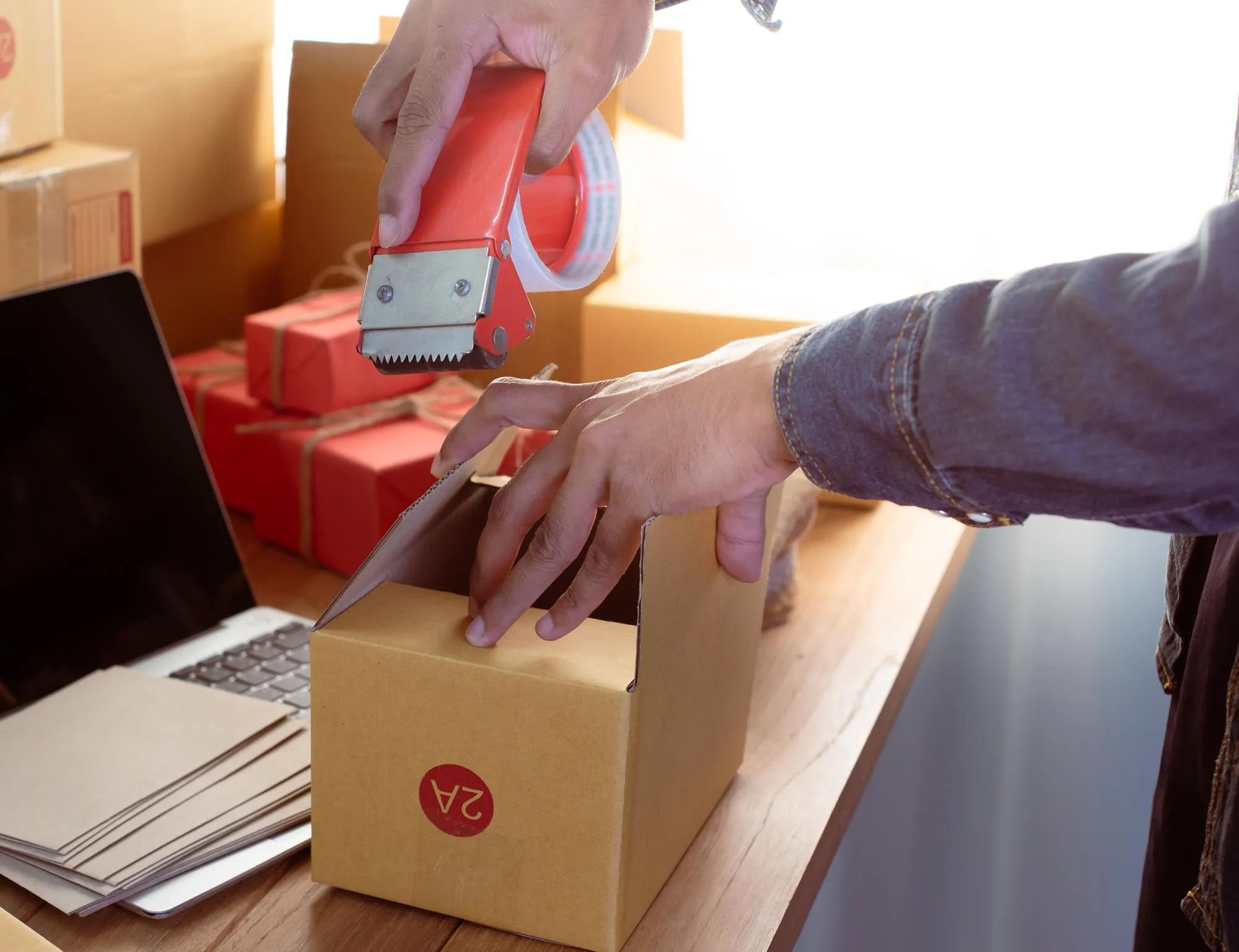Onlinehändler verpackt und versendet Bestellungen am Arbeitsplatz mit Laptop