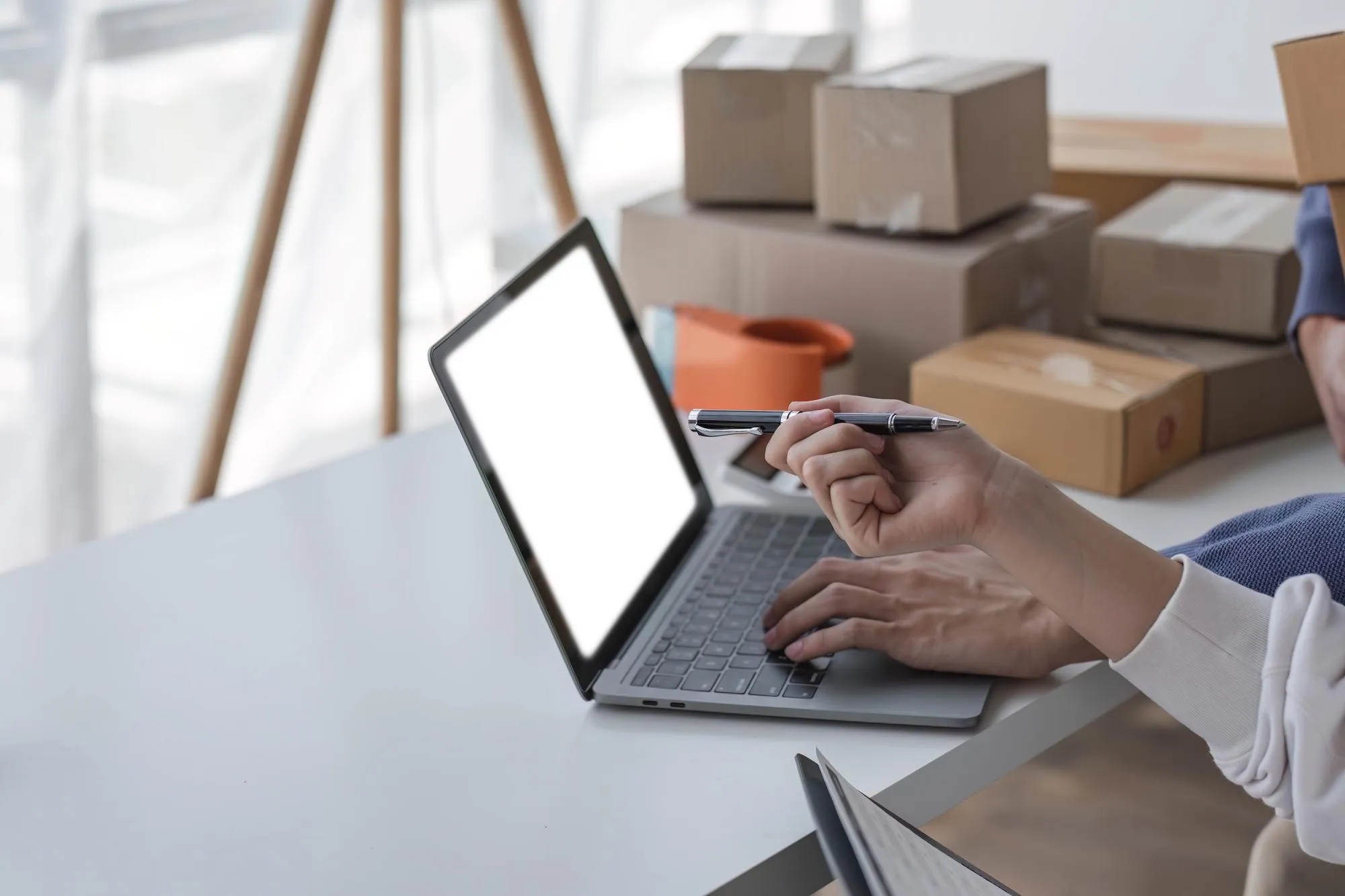Händlerin prüft Online-Bestellungen am Laptop zwischen Versandkartons