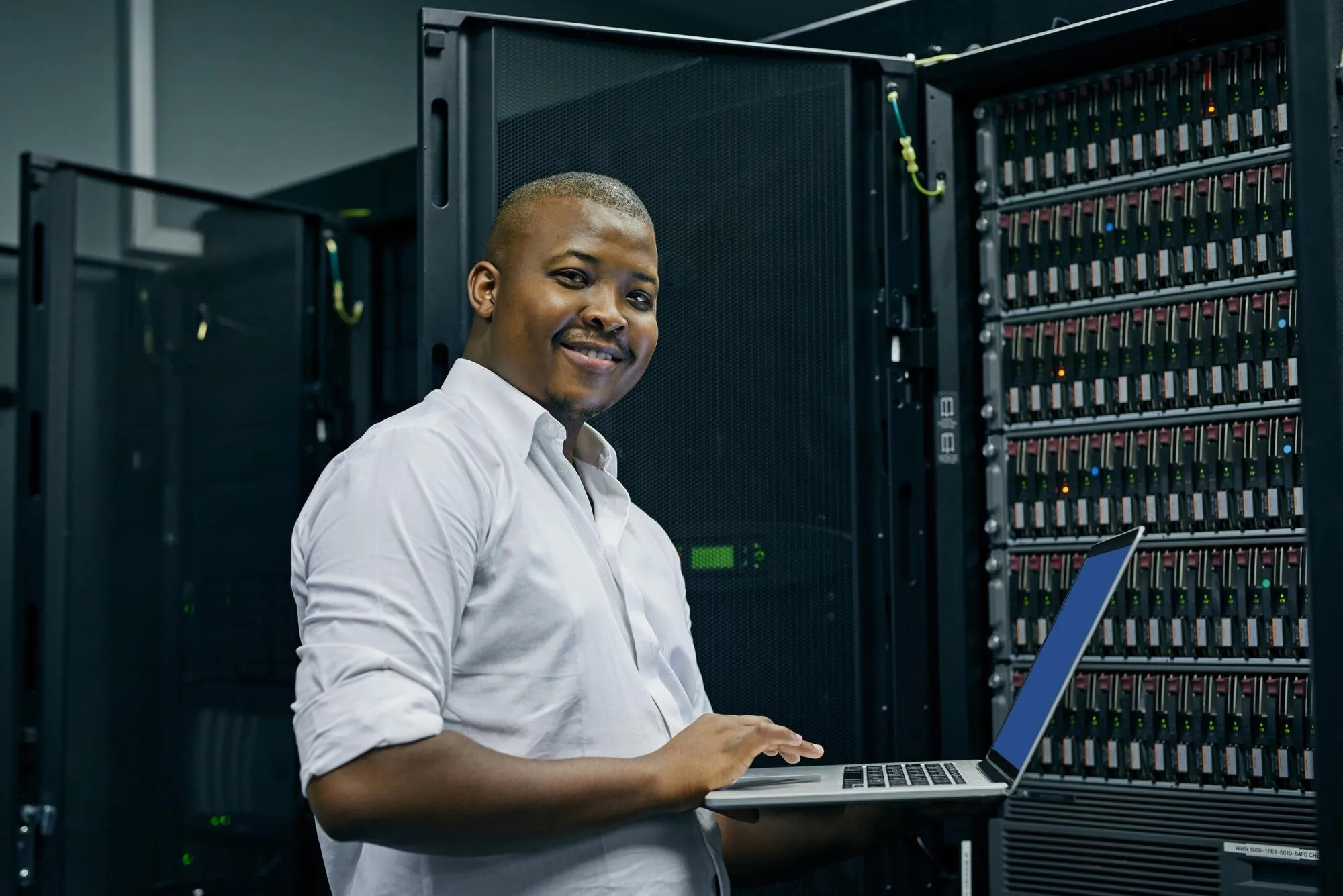 IT-Spezialist mit Notebook vor einem offenen Serverschrank im Rechenzentrum