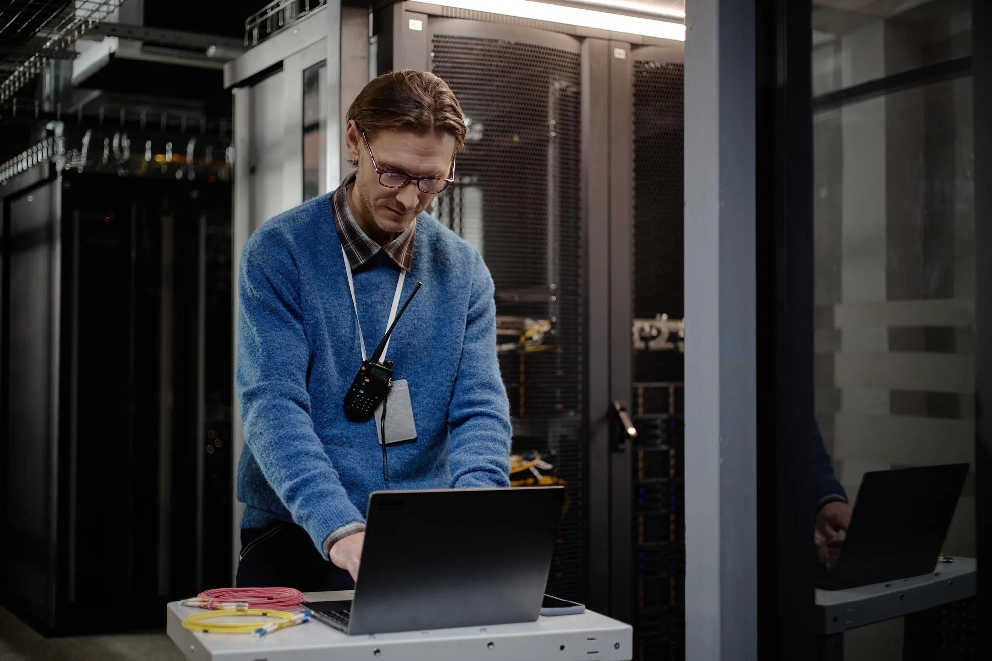 System Engineer bei der Server-Wartung am Laptop im Rechenzentrum, Glasfaser-Netzwerkkabel im Vordergrund