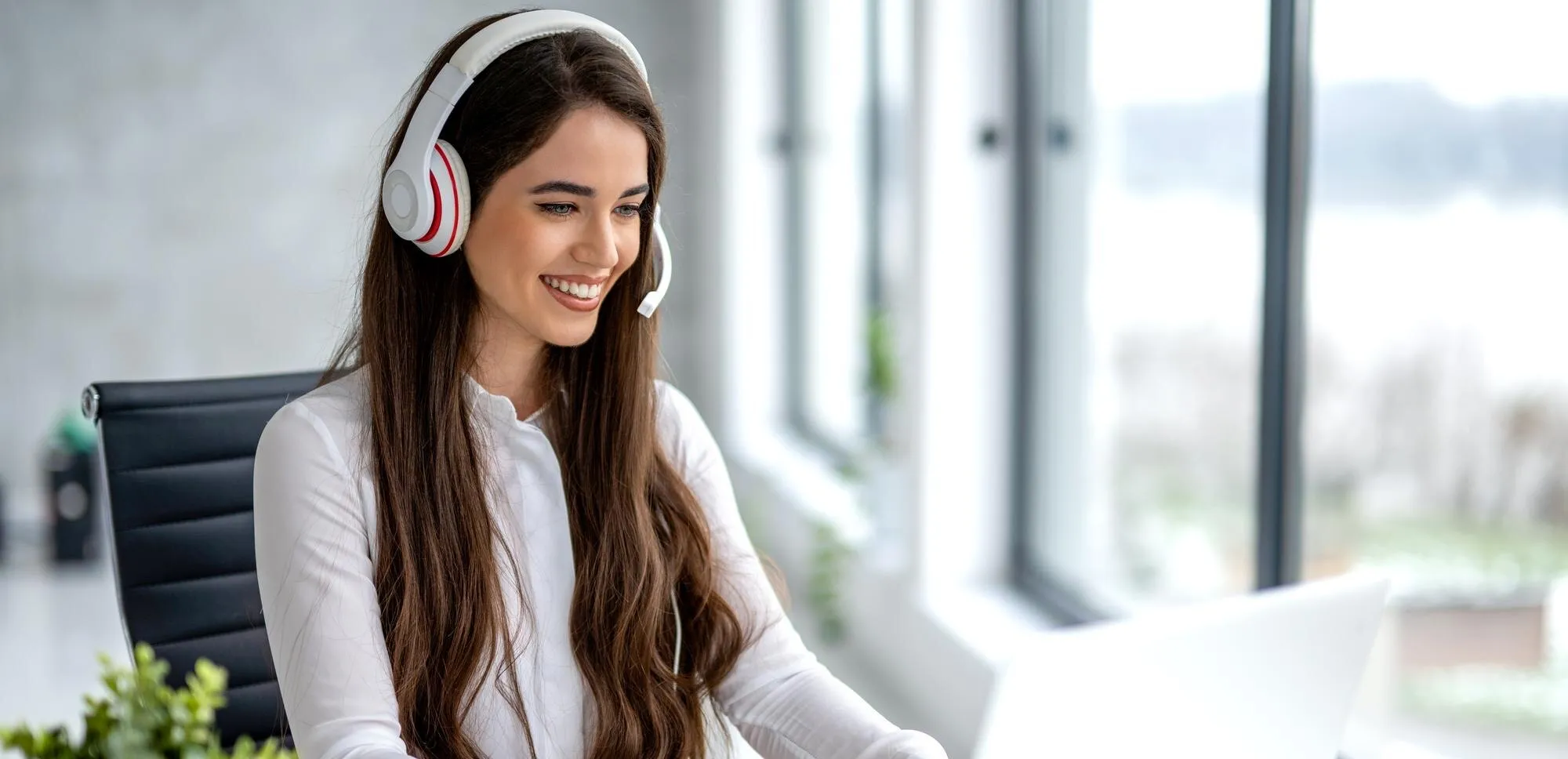 Kundenberaterin mit Headset am modernen, hellen Schreibtisch beim Telefonat